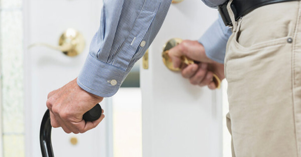 Older man opening a door, walking with assistance of a cane